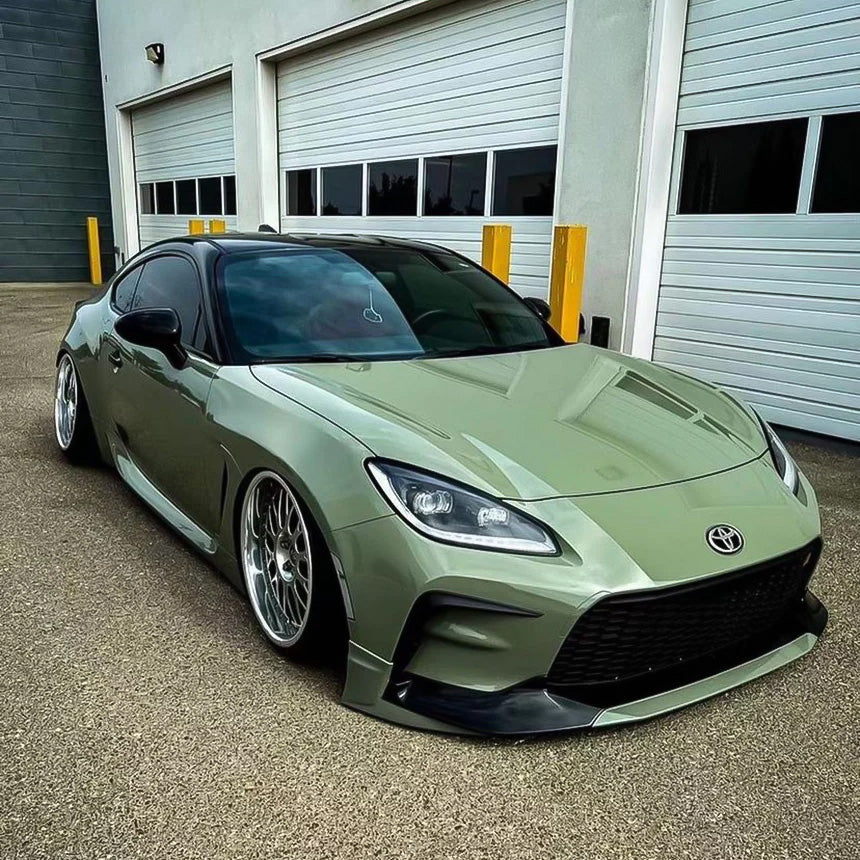 Front-side view of Toyota GR86 wrapped in TeckWrap Moss Green CG23-HD Glossy Vinyl, highlighting aggressive styling and smooth olive tone.
