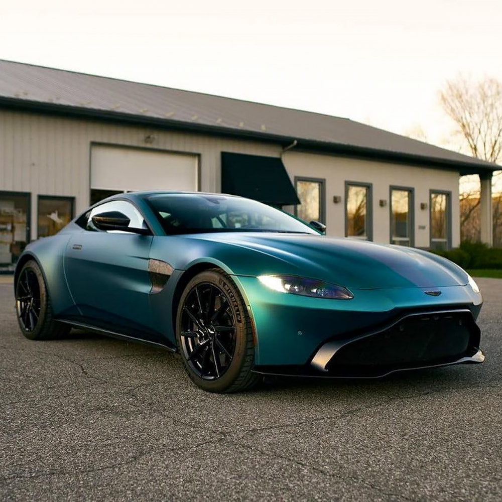 Aston Martin sports car fully wrapped in TeckWrap Jewel Green (SMT16) Satin Metallic vinyl, parked outside a garage with a deep emerald-blue matte finish.