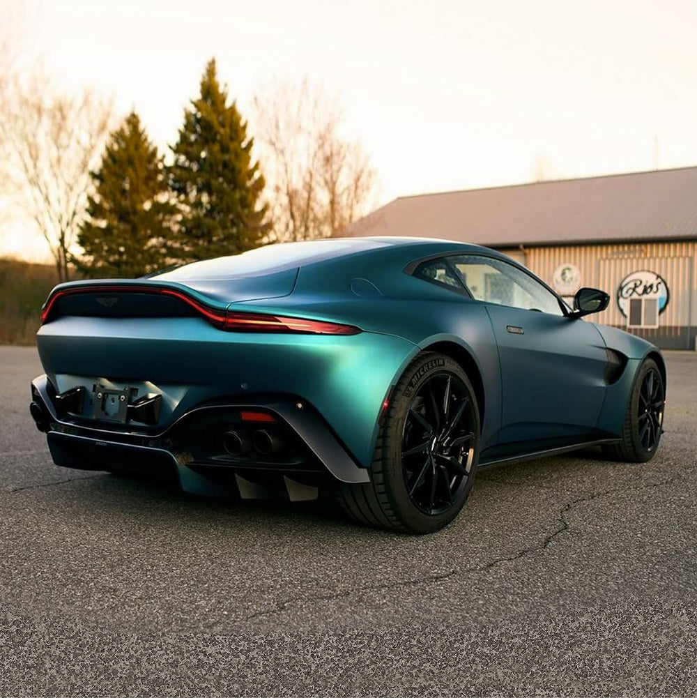 Rear angle view of an Aston Martin wrapped in Jewel Green (SMT16) Satin Metallic vinyl by TeckWrap, showing the satin texture and striking turquoise-blue hues under natural light.