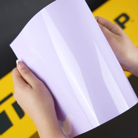 Hands holding a high-gloss CG48-HD Spanish Lavender vinyl wrap sample by TeckWrap, showcasing its smooth, reflective surface and soft purple color—ideal for car wrapping demonstrations.