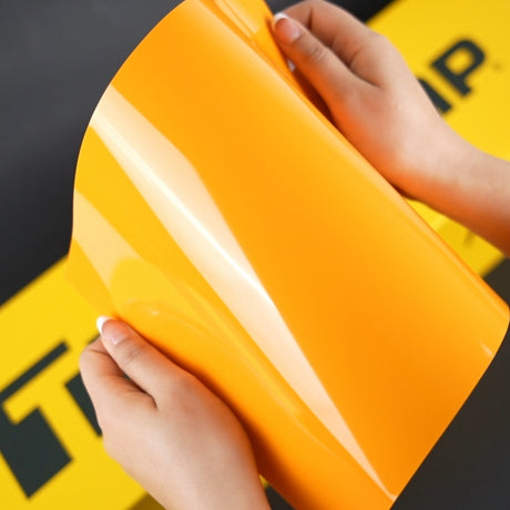 Hands holding Papaya Orange glossy vinyl wrap sample – Close-up of a person examining TeckWrap CG54-HD Papaya Orange vinyl film, highlighting its flexibility and reflective gloss.