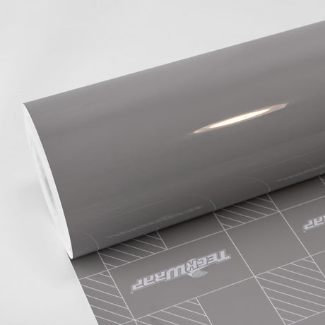 Wild Dove (CG55-HD) Vinyl Wrap by TeckWrap – a high-gloss automotive wrap in a sleek, refined grey shade, shown partially unrolled with a smooth, reflective surface and precision-cut backing paper for easy application.