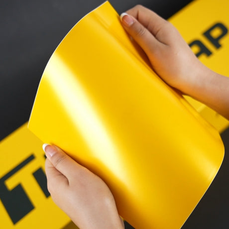Hands holding a sheet of TeckWrap Hornet Yellow (ECH16) Satin Vinyl Wrap, highlighting its bright, smooth satin texture and flexibility — perfect for seamless application on any vehicle surface.