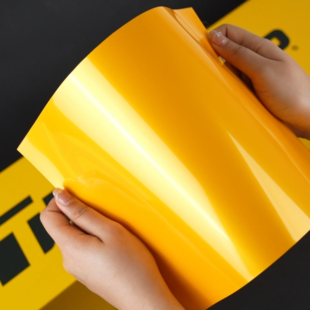 Close-up of hands holding glossy Golden Yellow (RB25-HD) vinyl wrap by TeckWrap, highlighting the vibrant and reflective finish.