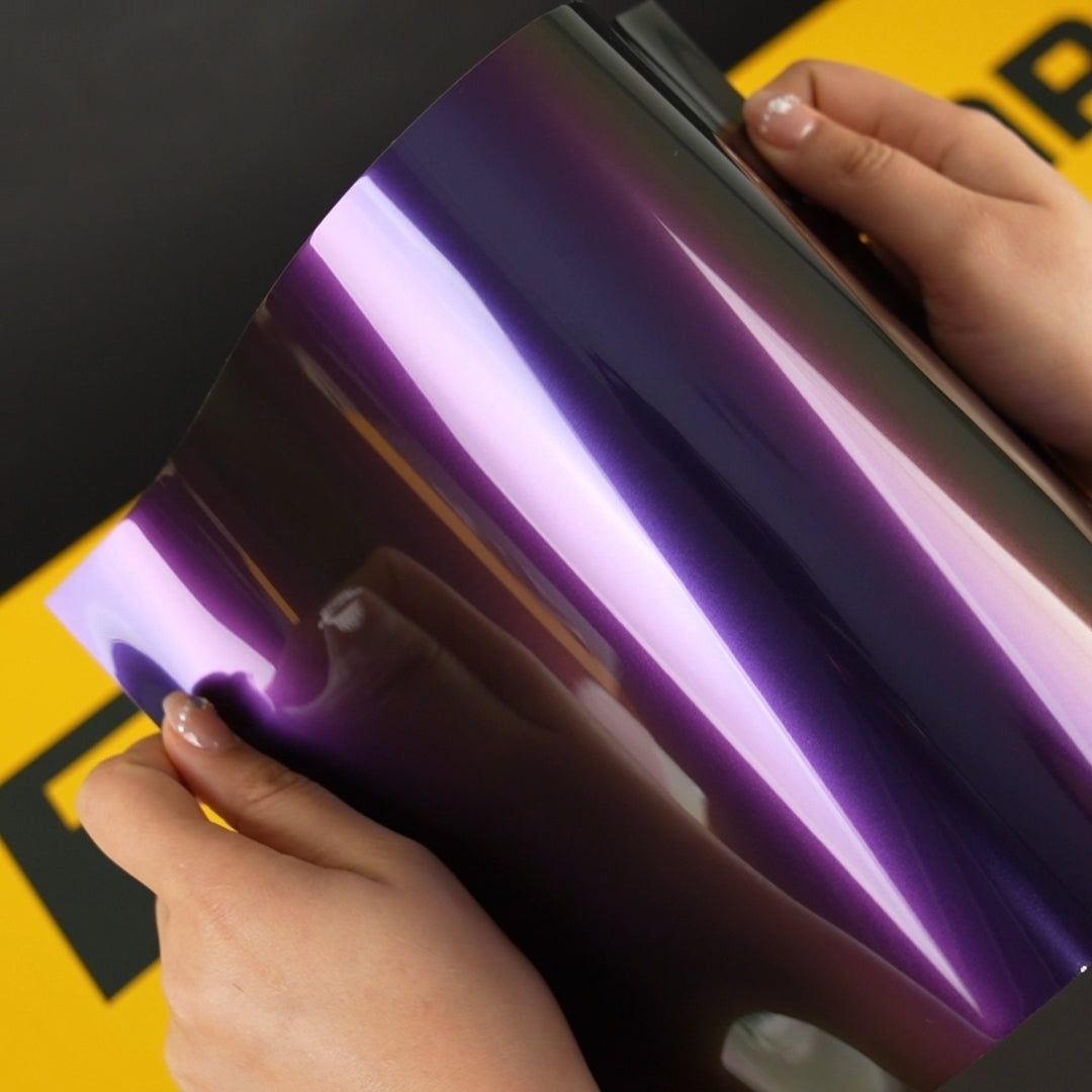 Hands holding A4 sample of TeckWrap RD19-HD Purple Green Rainbow Vinyl Wrap