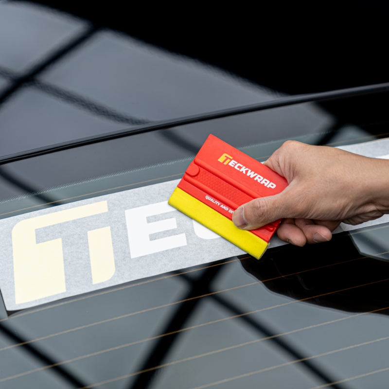 Hand smoothing TeckWrap decal on car glass using TeckWrap red and yellow squeegee