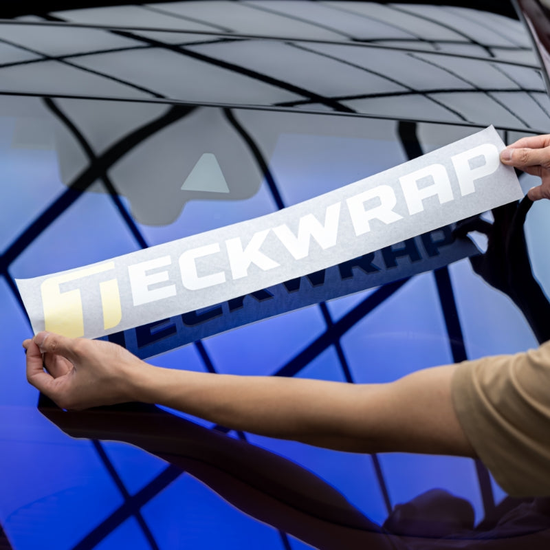 Applying TeckWrap logo decal on blue-tinted car window - step-by-step vinyl sticker installation