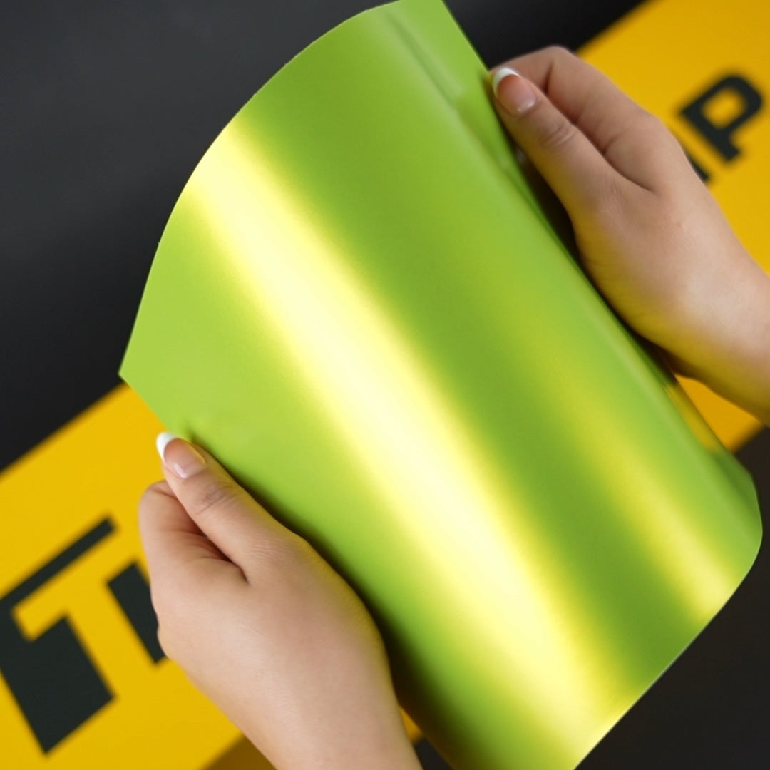 Close-up of Yellow Lime satin vinyl wrap sheet held in hands, showing smooth texture and vibrant green sheen