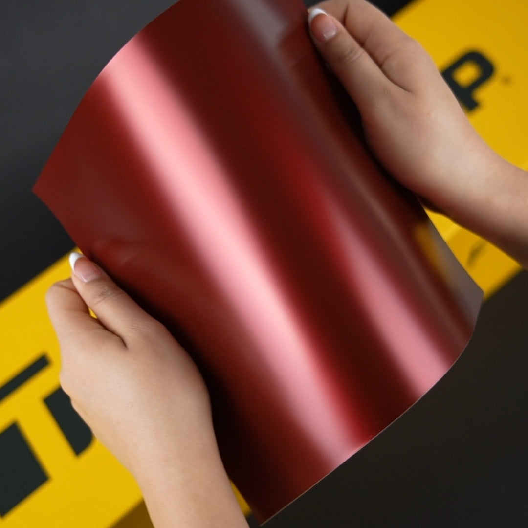 Hands holding TeckWrap A4 Samples of VCH422-S Sangria Red Satin Metallic Wrap
