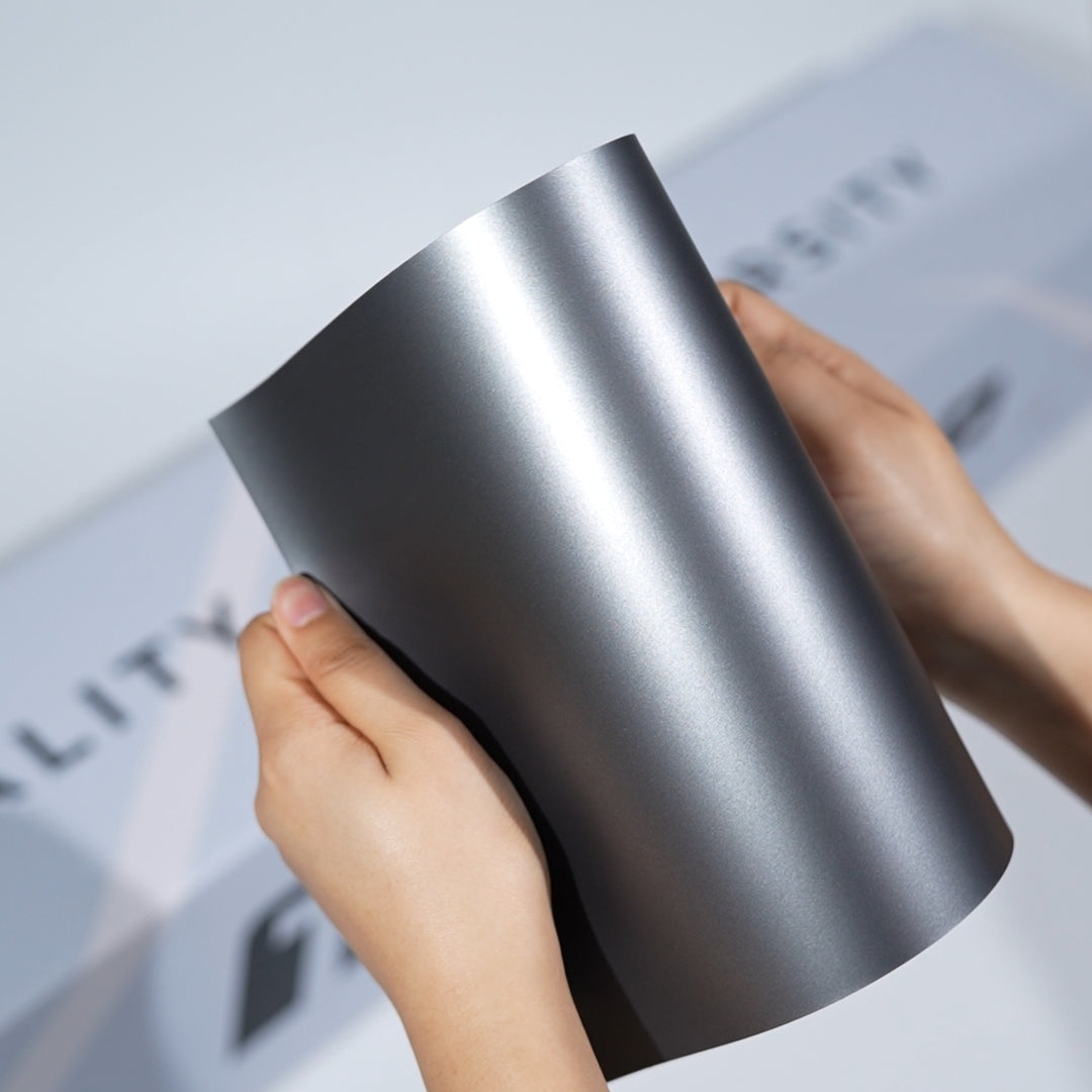 TeckWrap A5 Metallic Paint Protection Film sample in satin gunmetal grey with a bright silver center reflection