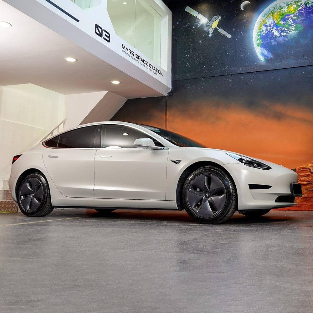 Tesla Model 3 fully wrapped in TeckWrap Granite Grey SCM47 satin chrome vinyl parked indoors against a mural backdrop for premium aesthetic enhancement