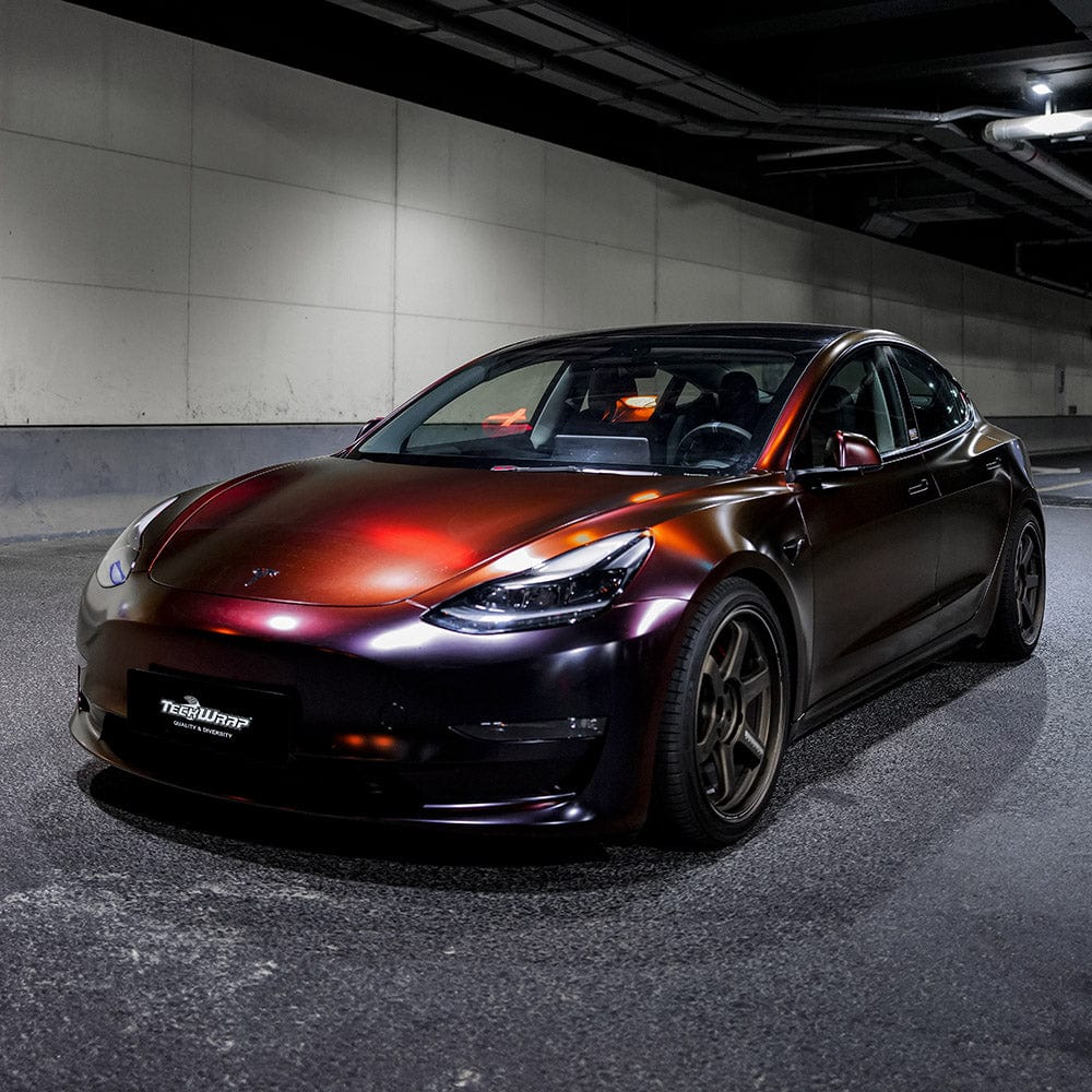Tesla Model 3 wrapped in TeckWrap Madeira Red Matte vinyl, parked under tunnel lights revealing its chameleon red-purple tones.