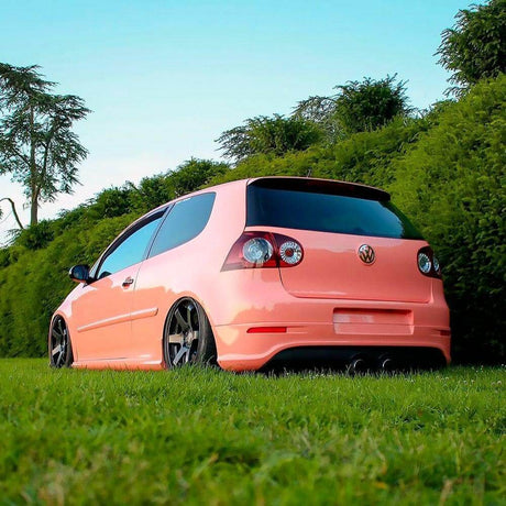Customized Volkswagen Golf featuring TeckWrap Gloss Amber Rose vinyl wrap, highlighted by its glossy finish and appealing peachy-pink color, parked in a lush green setting (CG36-HD).