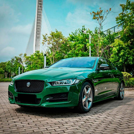 Elegant Jaguar sedan fully wrapped in TeckWrap Gloss Amphibian Green (CG32-HD), set against an urban greenery backdrop.