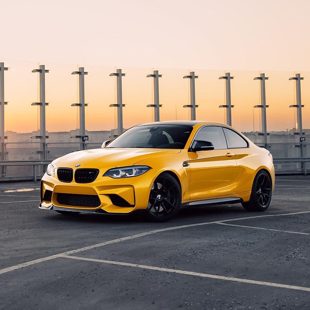 Stylish BMW wrapped in glossy Golden Yellow (RB25-HD) vinyl from TeckWrap, showcased against an urban sunset backdrop.