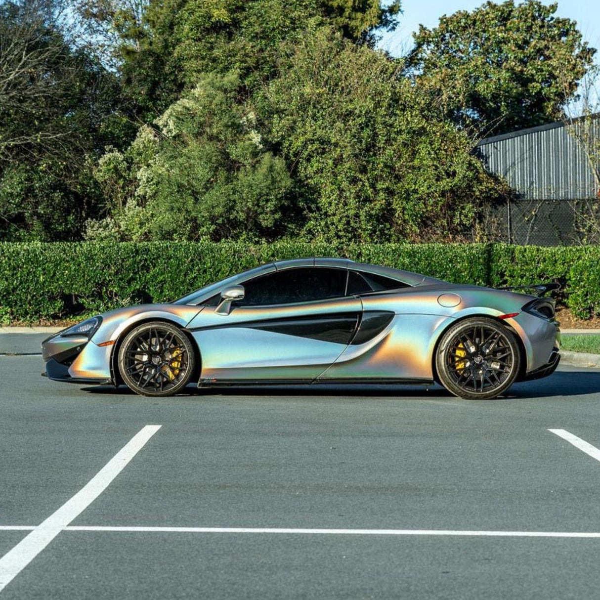 Side profile of a sleek sports car wrapped in TeckWrap Silver Fireworks Gloss Vinyl Wrap (RCH01-HD), displaying striking rainbow reflections and a premium glossy finish.