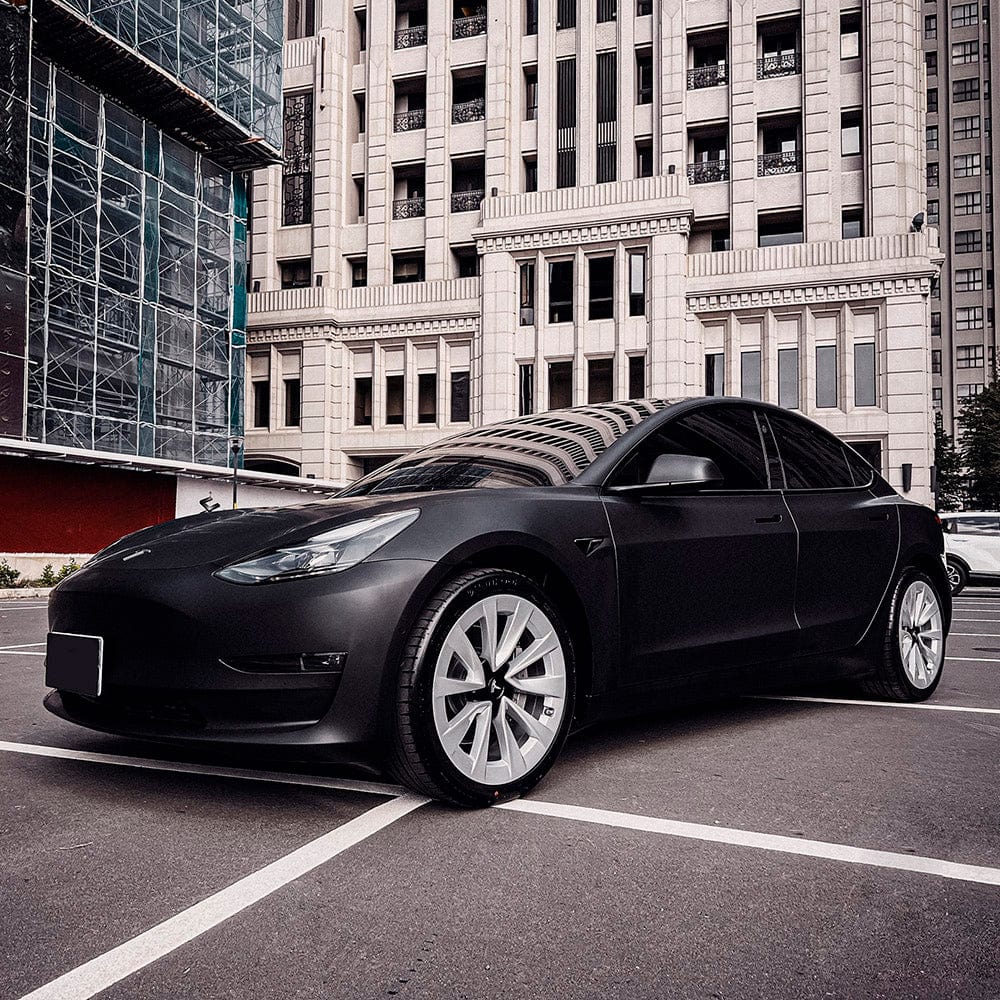 Tesla Model 3 wrapped in TeckWrap SCM01 Deep Black matte vinyl in front of urban skyscraper