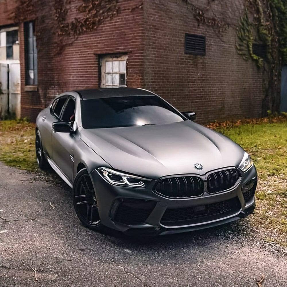 Angled front view of a BMW wrapped in TeckWrap Satin Black Silver (HM02-R) Vinyl Wrap near a brick building, emphasizing the vinyl's luxurious matte-silver sheen and sophisticated styling.