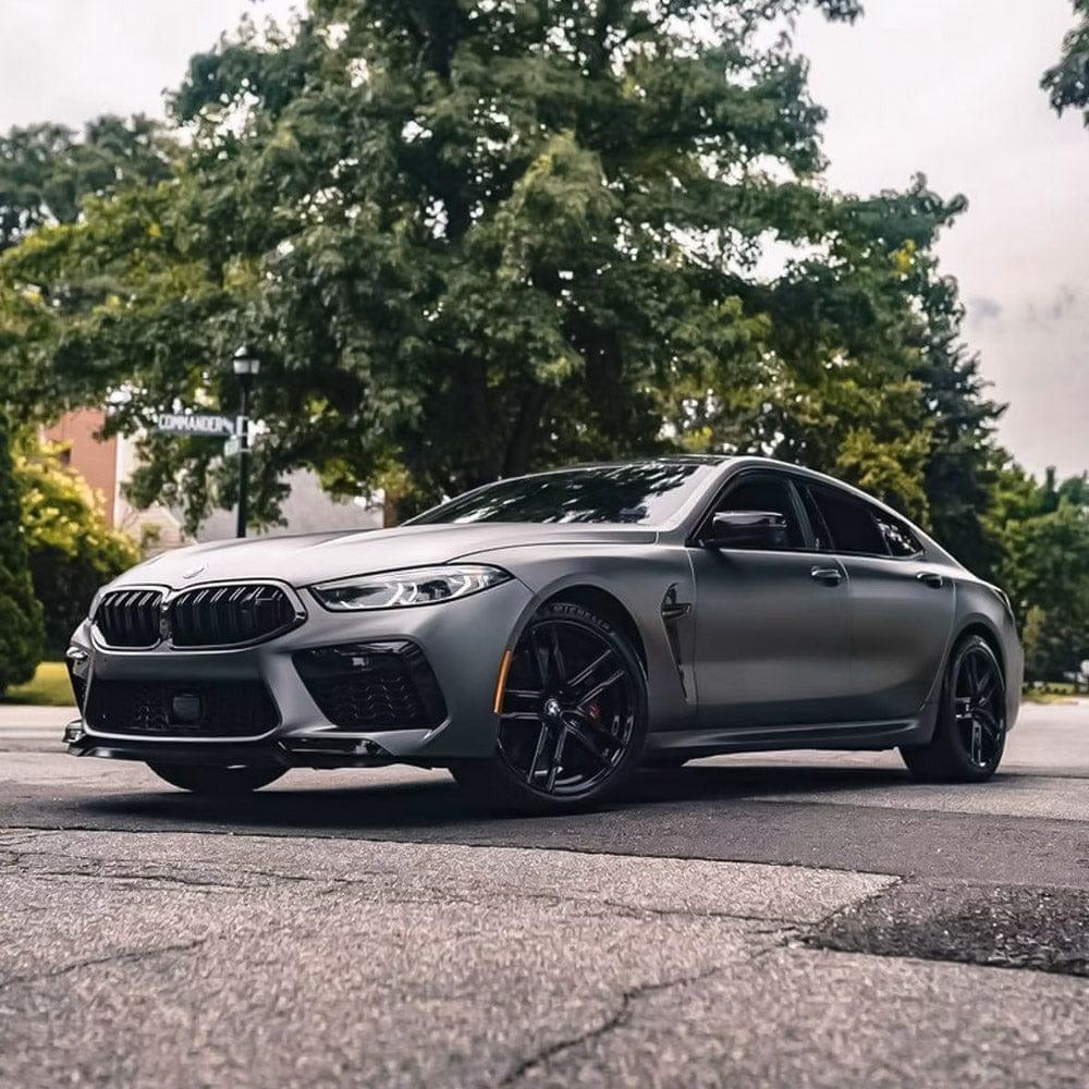 Side perspective of a BMW sedan fully wrapped in TeckWrap Satin Black Silver (HM02-R) Vinyl Wrap, parked on a street lined with greenery, capturing the refined, understated elegance of the wrap.