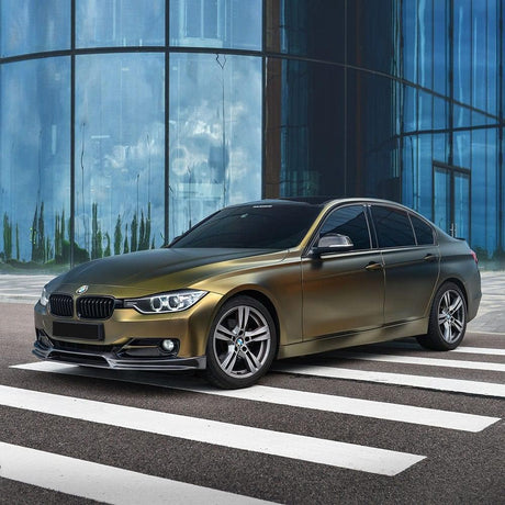 Side-angle view of a BMW elegantly wrapped in Teckwrap Satin Bond Gold (ECH17) vinyl wrap, set against a modern glass building, displaying a refined and upscale look.