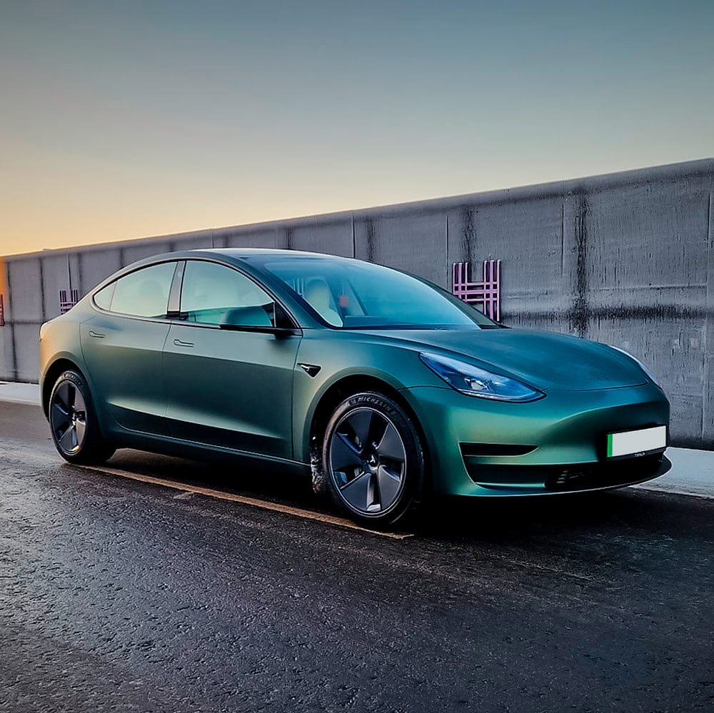 Side view of a Tesla wrapped in TeckWrap Pine Green Satin Vinyl, highlighting the elegant matte sheen at sunset.