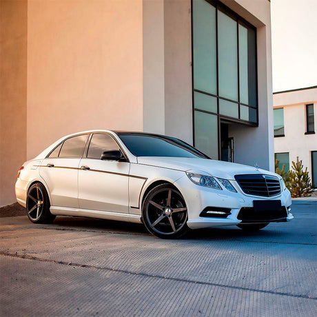 Side-angle view of a Mercedes-Benz elegantly wrapped in Teckwrap Satin Pearl White (ECH01) vinyl wrap, parked near a modern building, emphasizing its sophisticated satin pearl finish.