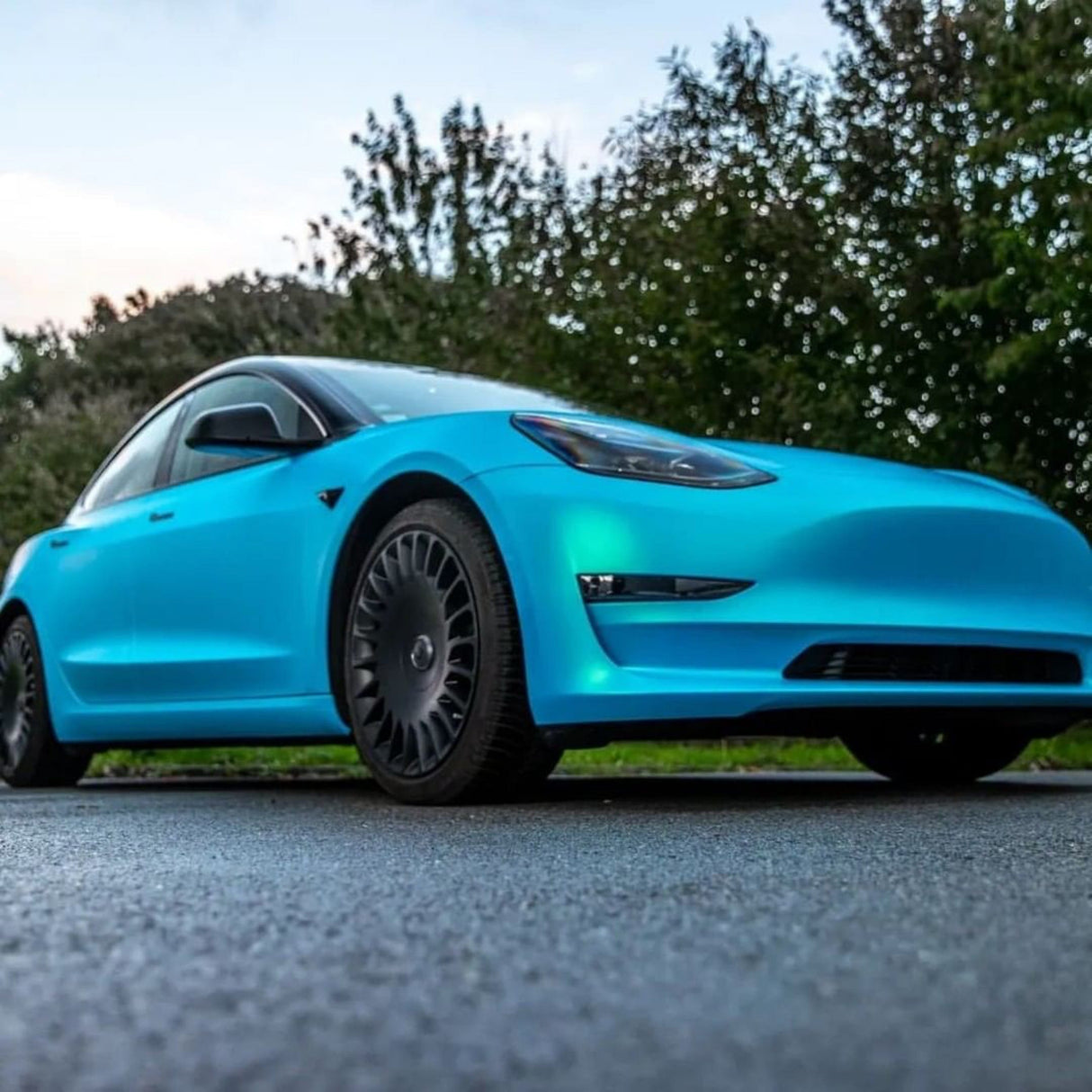 Dynamic Low-Angle Shot of Tesla Model 3 Featuring Full-Body TeckWrap Surf Blue (SMT11) Satin Vinyl Wrap, Highlighting its Satin Matte Surface and Enhanced Aesthetic Appeal