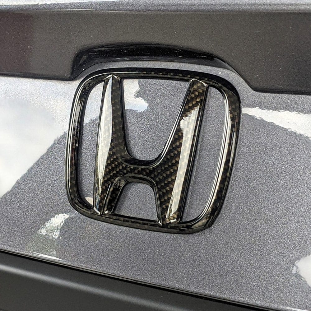 Honda logo emblem customized with Ceramic Carbon (RCF03) vinyl wrap, clearly displaying the elegant carbon fiber texture enhancing vehicle aesthetics.