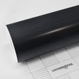 TeckWrap Pitch Black Carbon (CF02) structured vinyl wrap roll showcasing its refined carbon fiber texture for automotive styling.