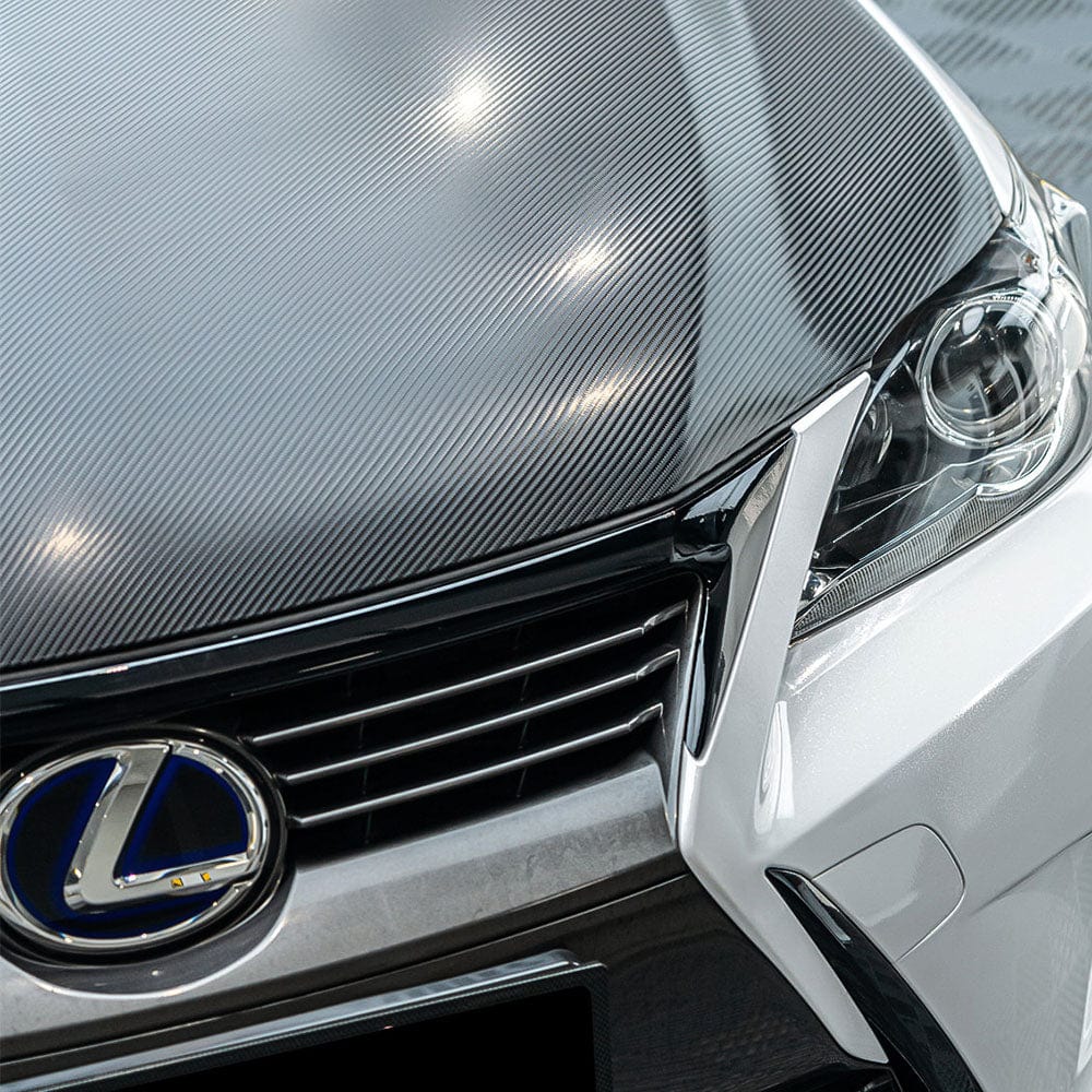 Front hood detail of a car wrapped in TeckWrap Pitch Black Carbon (CF02), illustrating the luxurious and realistic carbon fiber texture under light reflection.