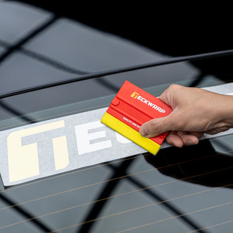 Hand smoothing TeckWrap decal on car glass using TeckWrap red and yellow squeegee