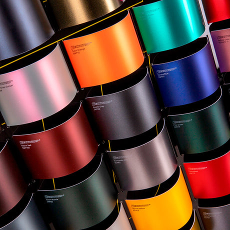 Colorful rolls of vinyl wrap samples with a brand name on a dark background