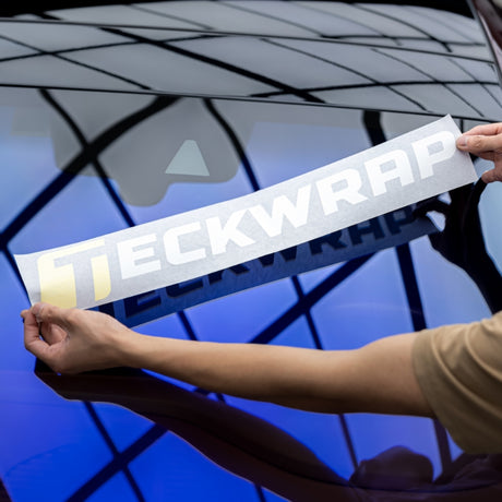 Applying TeckWrap logo decal on blue-tinted car window - step-by-step vinyl sticker installation