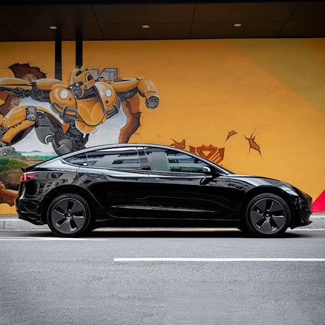 Tesla Model 3 fully wrapped in TeckWrap Black Gloss (CG01) vinyl, showcasing a sleek, polished exterior parked against a vibrant mural wall