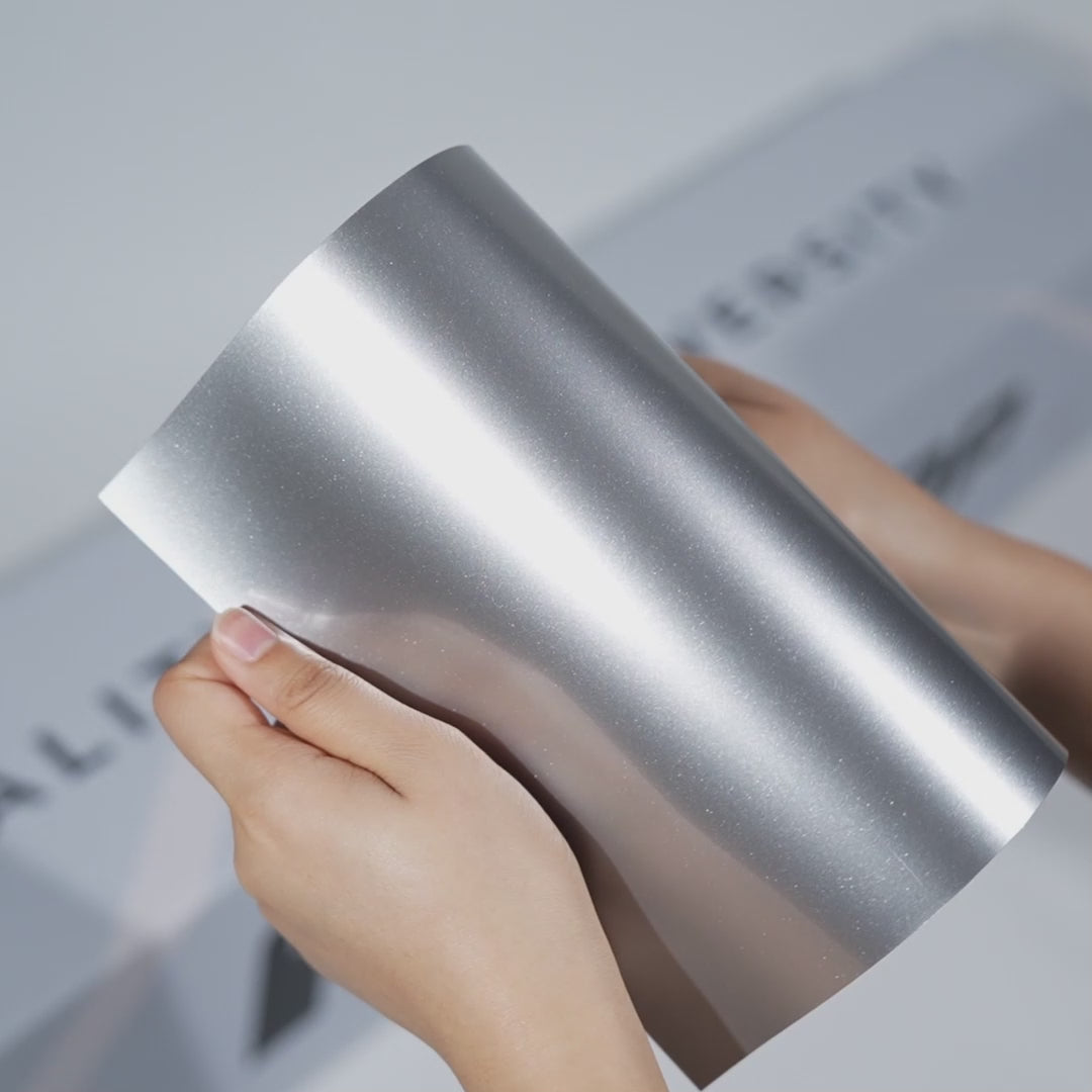 Hands holding a TeckWrap Stellar Silver Metallic PPF sample (CPX406), highlighting its bright glossy silver metallic finish and premium paint protection surface.