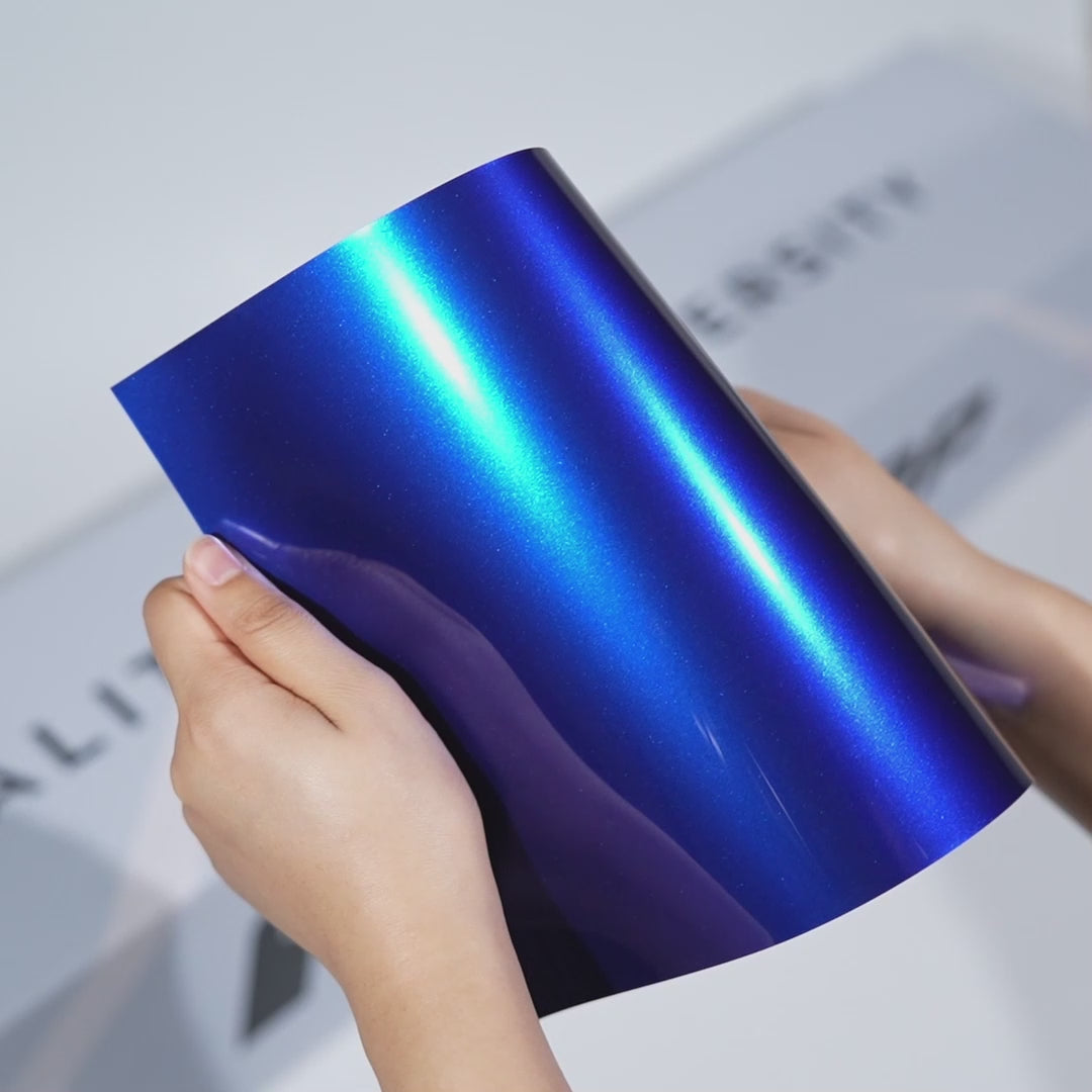Hands holding a TeckWrap Sapphire Blue Gloss Color PPF sample (CPX501), displaying its deep jewel-tone blue shine and premium paint protection finish.