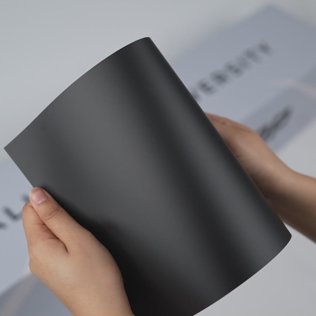 Hands holding a TeckWrap Velour Black Matte Color PPF sample (CPX301M), showcasing its smooth matte black finish and premium paint protection surface.