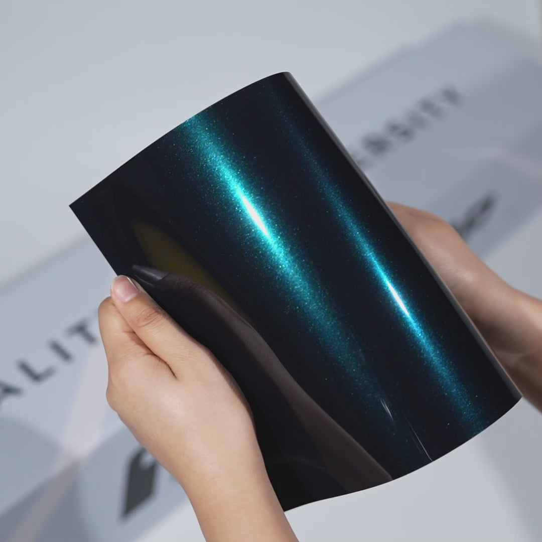 Hands holding a TeckWrap Nordic Green Metallic PPF sample (CPX411), highlighting its deep glossy teal-green metallic finish and premium paint protection surface.
