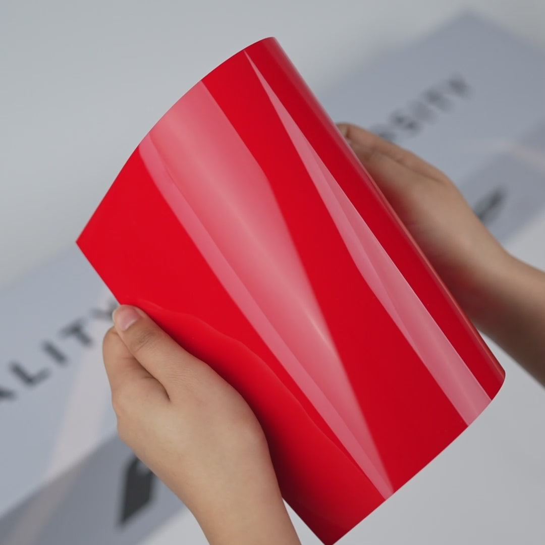 Hands holding a TeckWrap Inferno Red Gloss Color PPF sample (CPX311), showcasing its bold glossy red finish and premium paint protection surface.