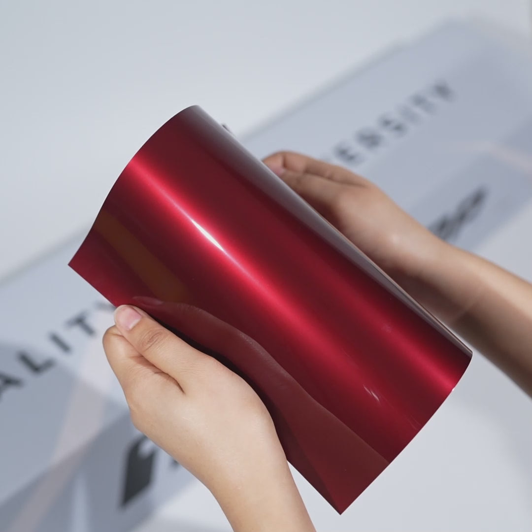 Hands holding a TeckWrap Dark Carmine Metallic PPF sample (CPX416), highlighting its glossy crimson-red metallic finish and premium paint protection surface.