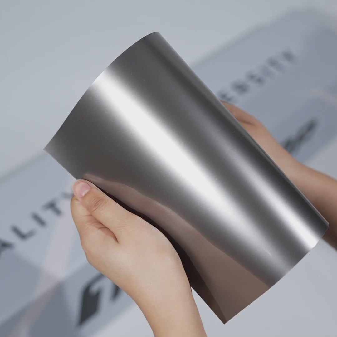 Hands holding a TeckWrap Lustrous Silver Metallic PPF sample (CPX407), showcasing its deep glossy silver metallic finish and premium paint protection surface.
