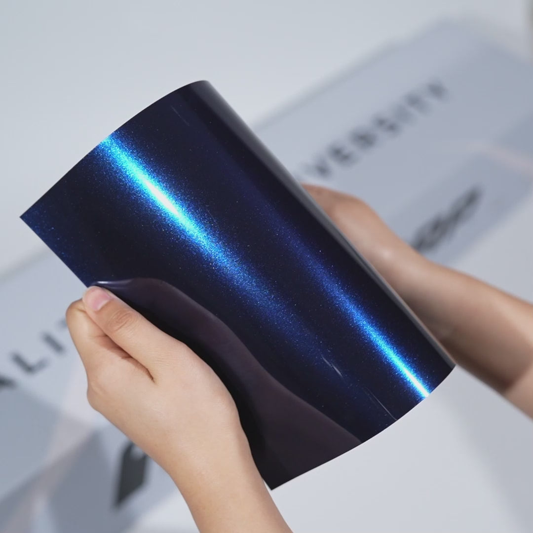 Hands holding a TeckWrap Abyss Blue Metallic PPF sample (CPX417), showcasing its deep sapphire metallic gloss and premium paint protection finish.