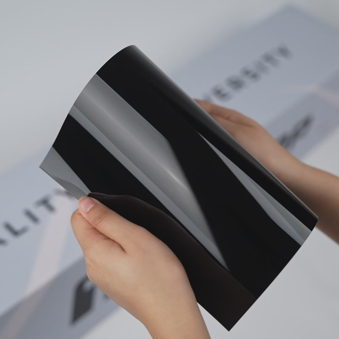 Hands holding a TeckWrap True Black Gloss Color PPF sample (CPX301), showcasing its deep glossy black finish and premium paint protection surface.