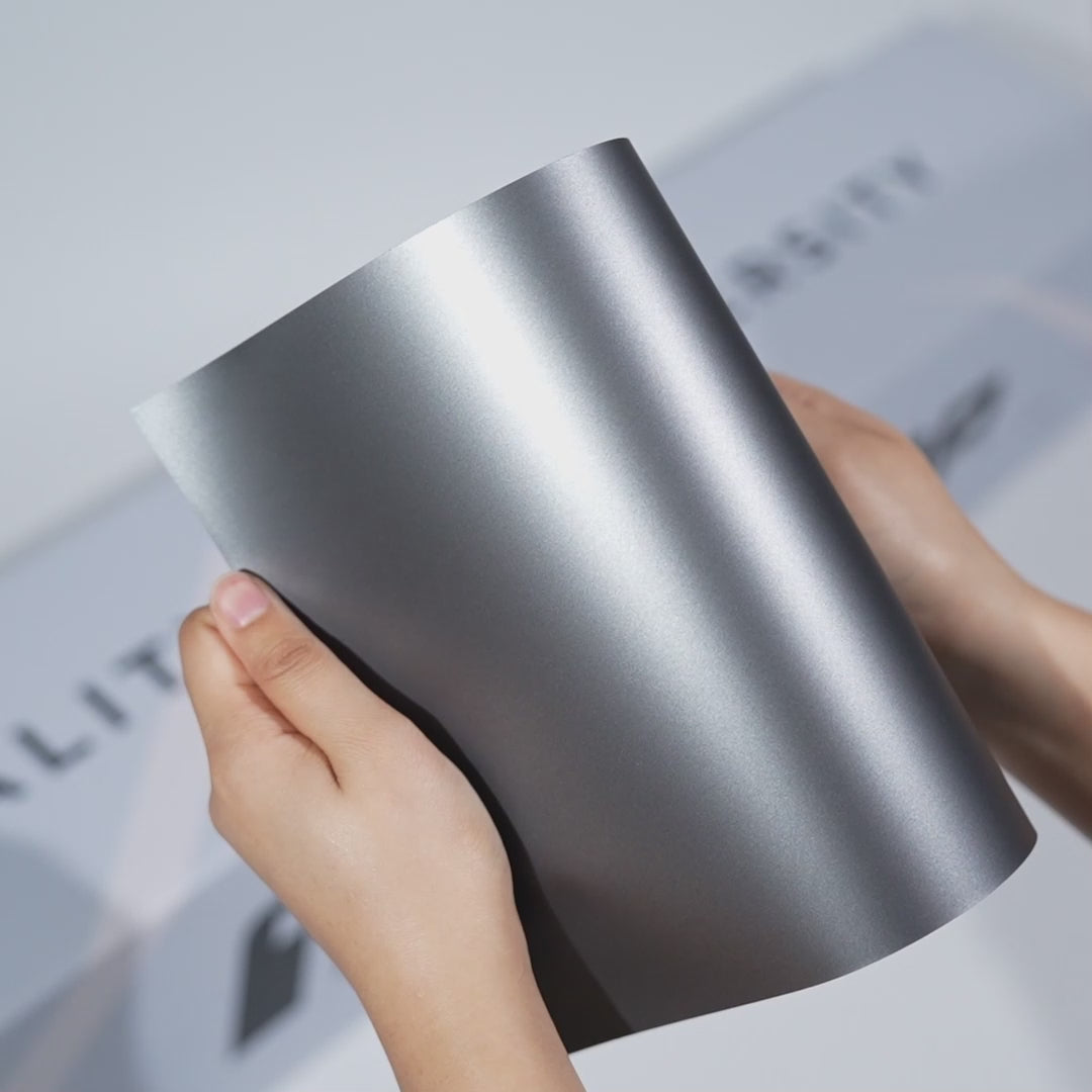 Hands holding a TeckWrap Silk Ash Matte Grey PPF sample (CPX419M), highlighting its smooth satin grey finish and premium matte paint protection surface.