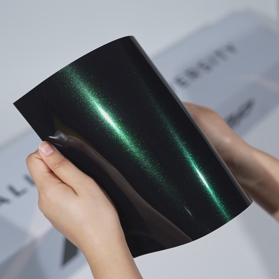 Hands holding a TeckWrap Warm Emerald Metallic PPF sample (CPX412), showcasing its vivid emerald-green metallic gloss and premium paint protection finish.
