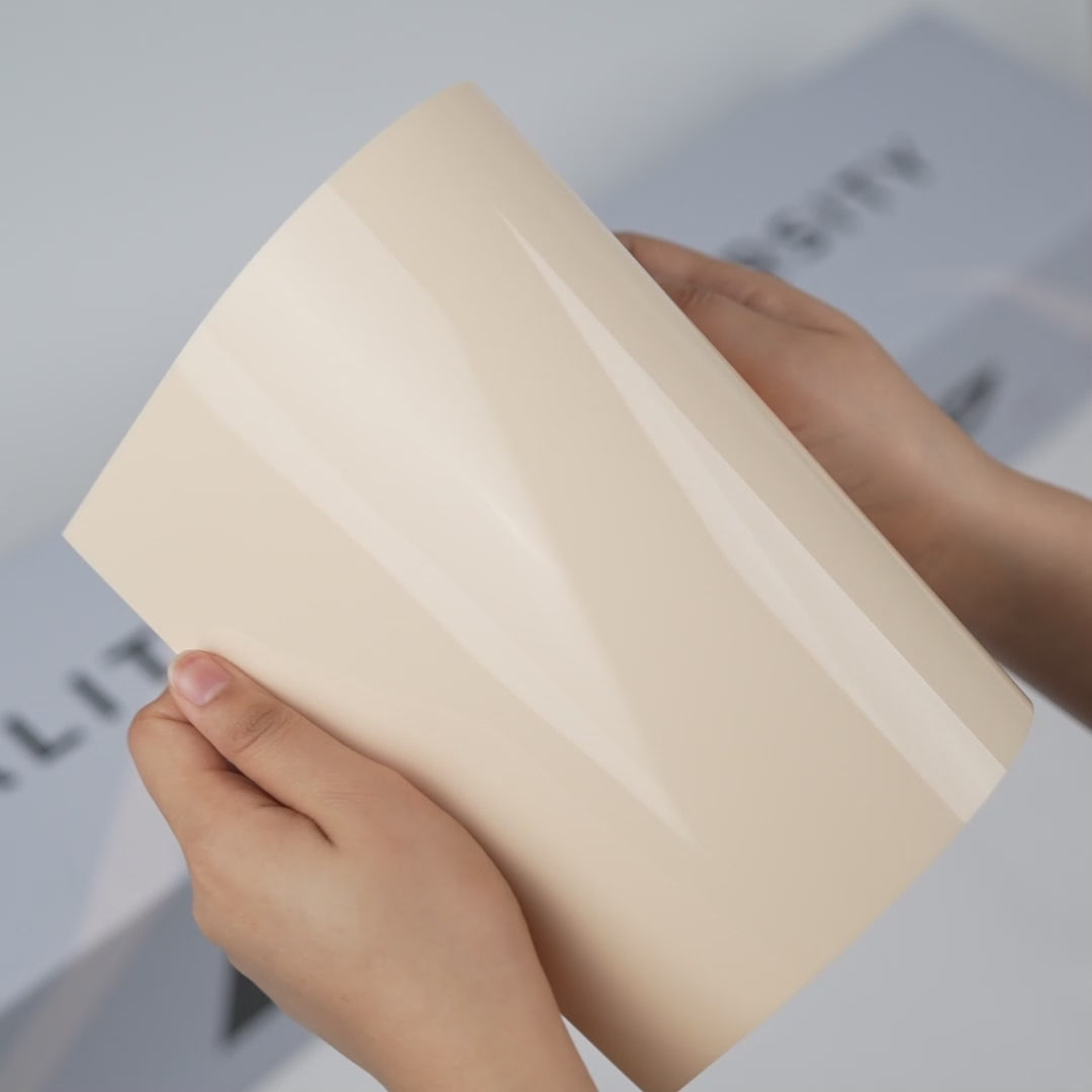 Hands holding a TeckWrap Almond White Gloss Color PPF sample (CPX303), showcasing its smooth glossy almond-white finish and premium paint protection surface.