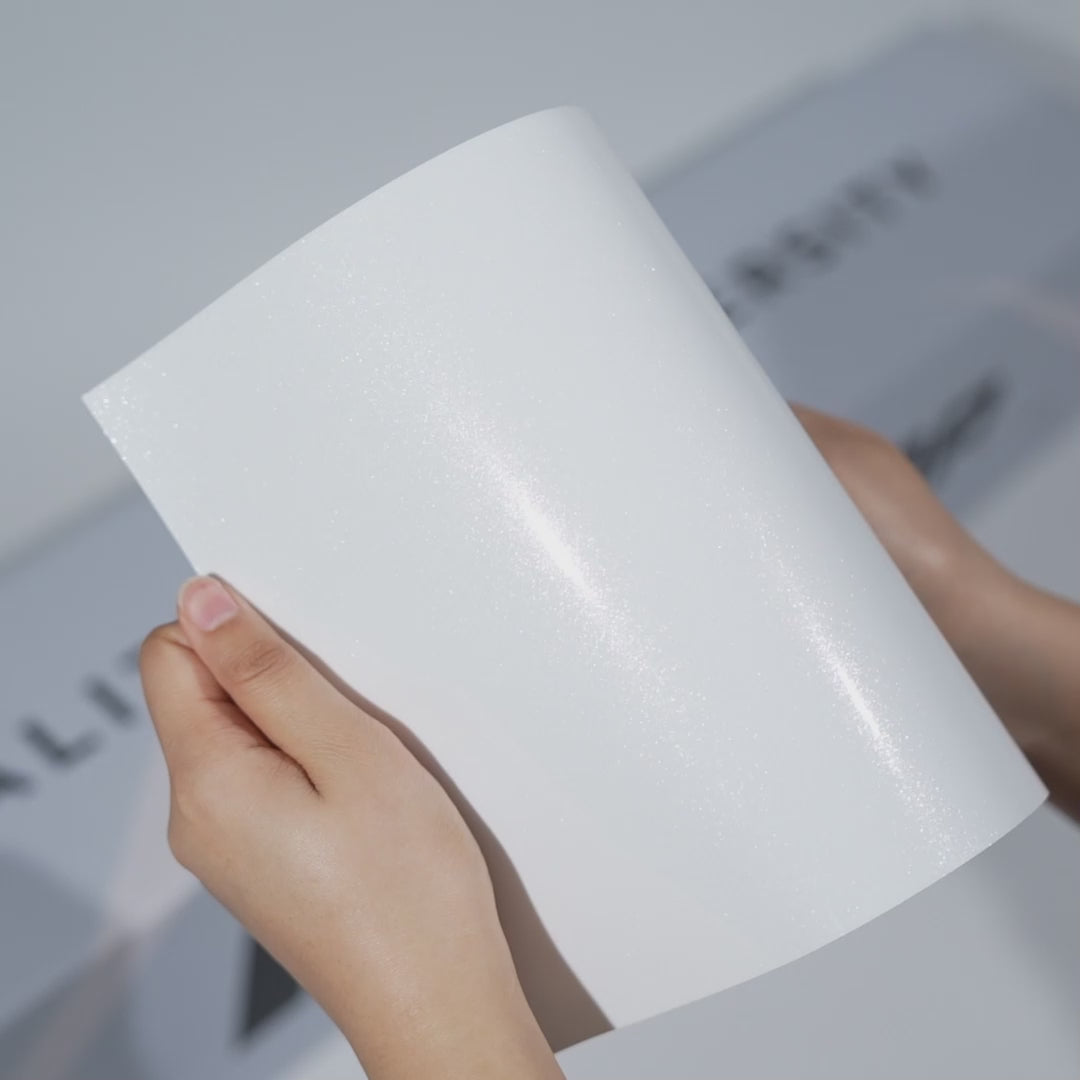 Hands holding a TeckWrap Sparkling White Pearl PPF sample (CPX402), highlighting its glossy metallic white pearl shimmer and premium paint protection surface.