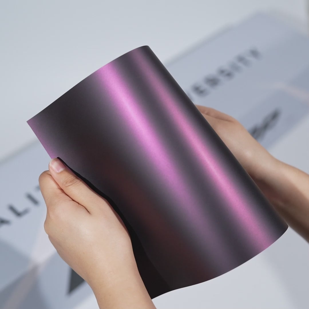 Hands holding a TeckWrap Graphite Rose Matte PPF sample (CPX420M), showcasing its satin violet-grey finish and premium matte paint protection texture.