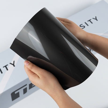 TeckWrap A5 Paint Protection Film sample in glossy smoke black with mirror-like reflections on the curved sheet