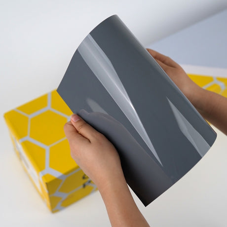 Dark grey TeckWrap A5 Pure Color Paint Protection Film sample with yellow box background
